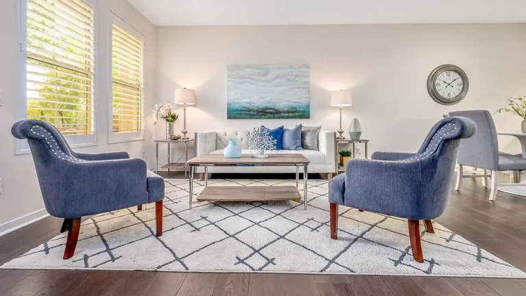 How to choose an area rug: size, material and placement Blue armchairs and a white sofa arranged on a geometric area rug in a bright living room